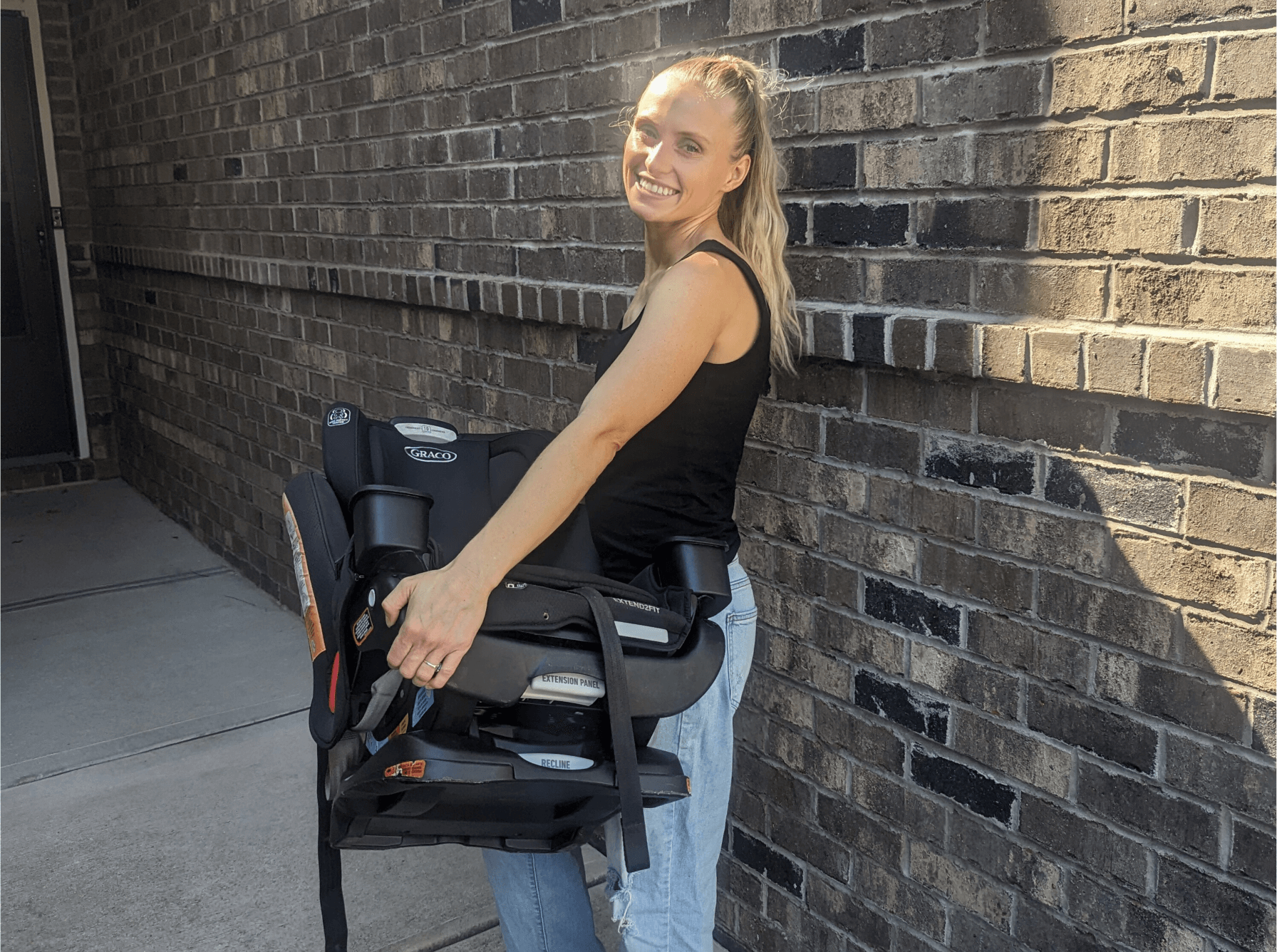 Janie Kokakis, founder of Little Reset, smiling while holding a clean Graco child car seat outside in Cary, NC.